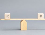 A wooden balance scale weighing a block marked with a head-and-brain icon against a block marked with a medical caduceus