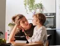 A mother and her son looking at each other across a kitchen table with a tablet