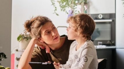 A mother and her son looking at each other across a kitchen table with a tablet