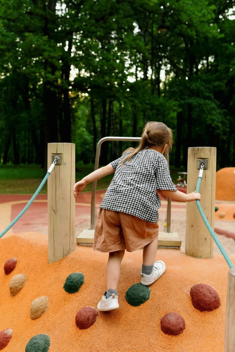 A child crossing a rope bridge on a playground climbing frame, seen from behind