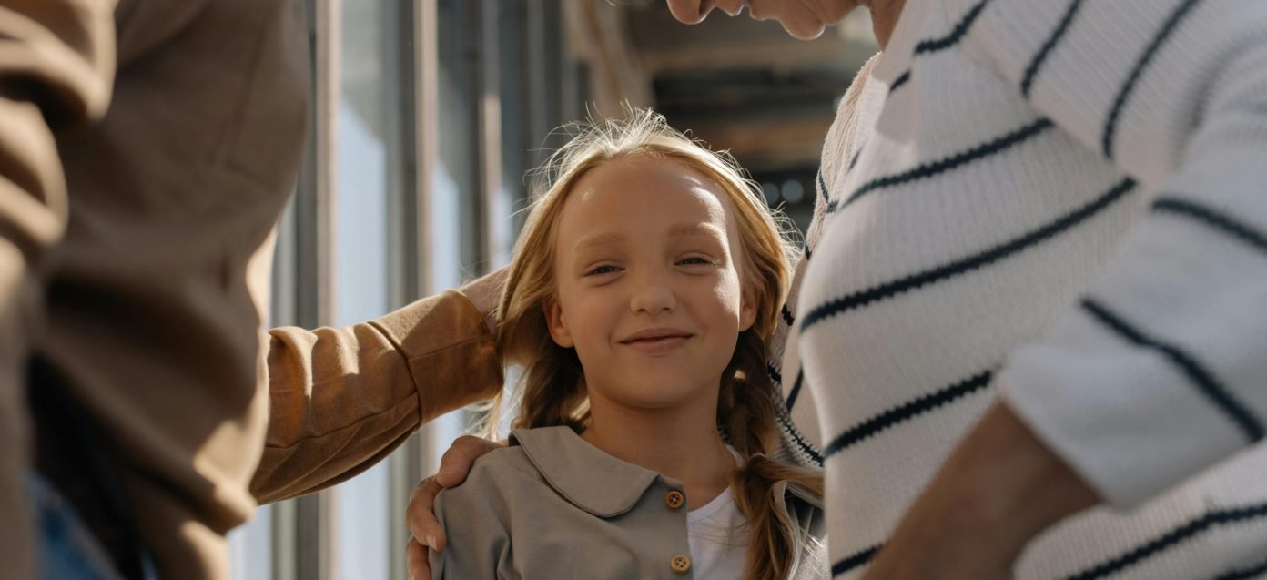 A smiling girl looking up at her two grandparents, who rest their hands on her shoulders
