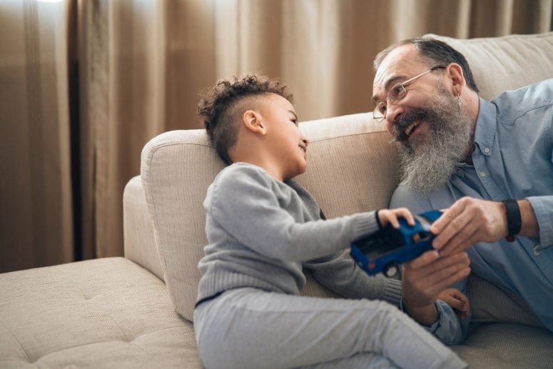 A grandfather and a small boy playing with a blue toy car on a sofa