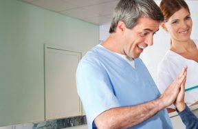 A man giving a boy a high five in a hospital corridor while two nurses look on