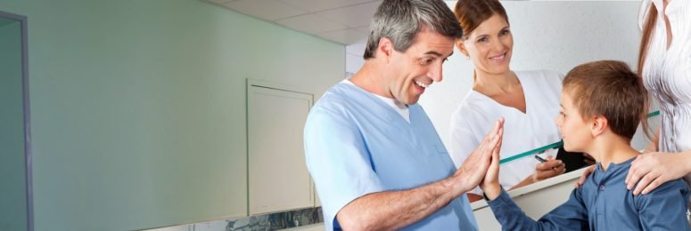 A man giving a boy a high five in a hospital corridor while two nurses look on
