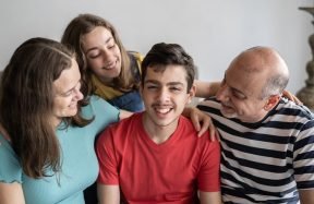 A grandfather, mother, daughter and teenage son laughing together on a sofa