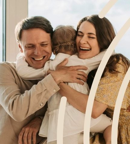 A father and mother hugging their small daughter beside a window