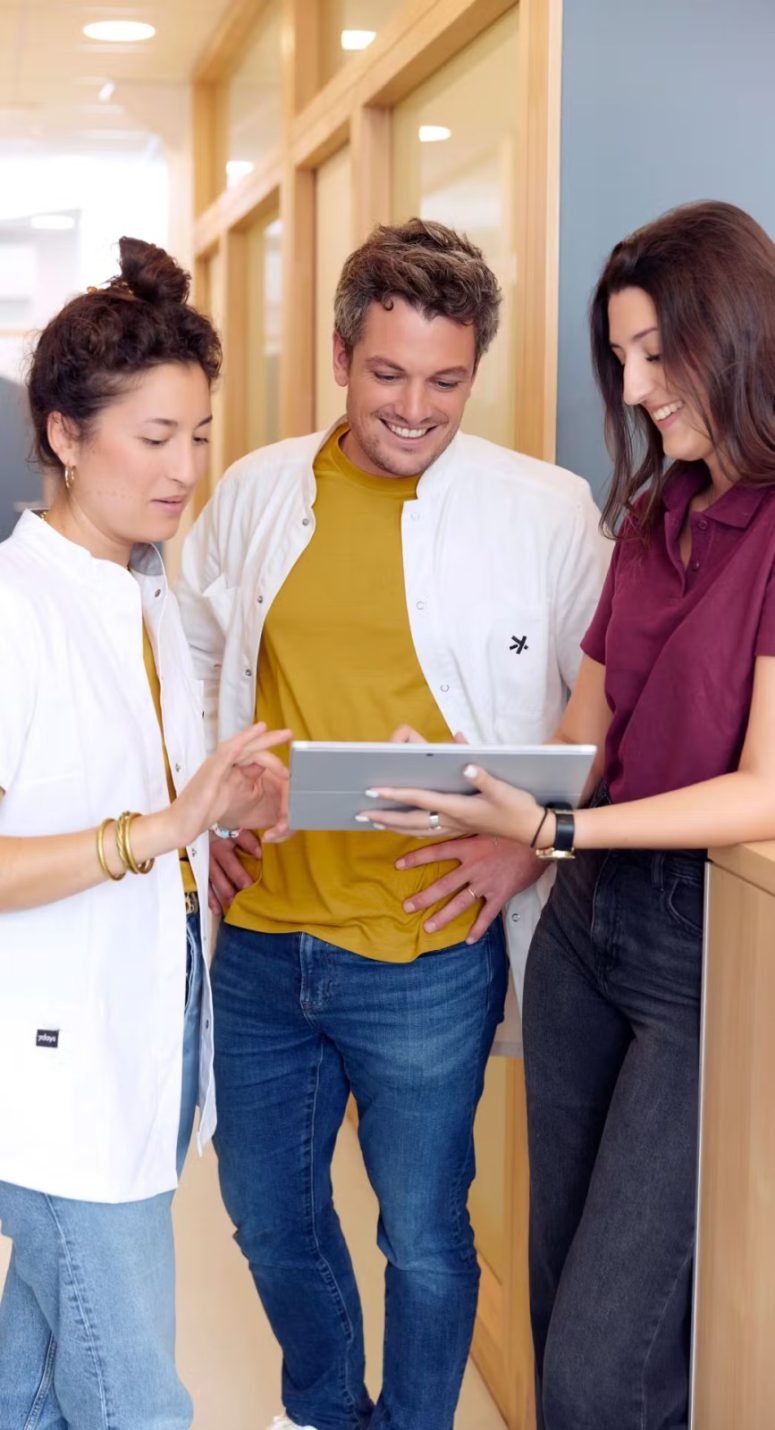 Three colleagues looking together at a tablet in a bright corridor
