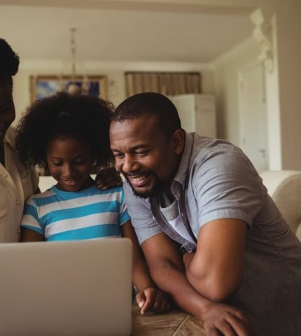 A mother, father and their young daughter smiling at a laptop on the sofa